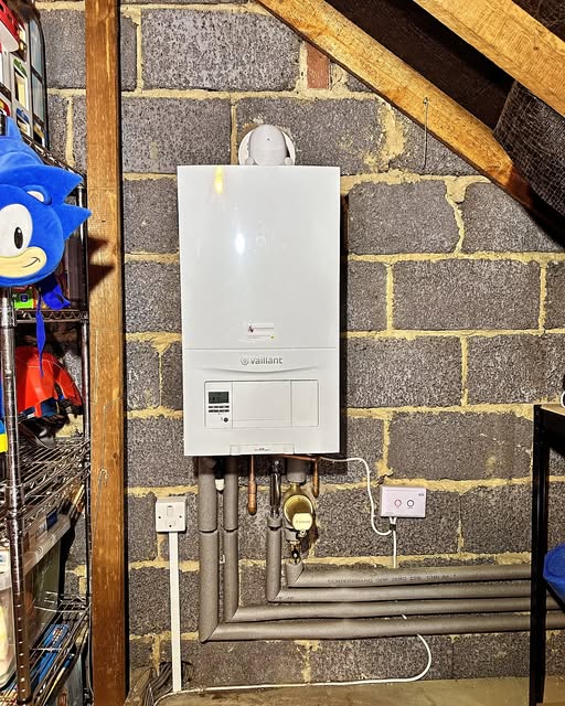 A boiler installed against exposed brickwork in a loft space, with copper pipework running below
